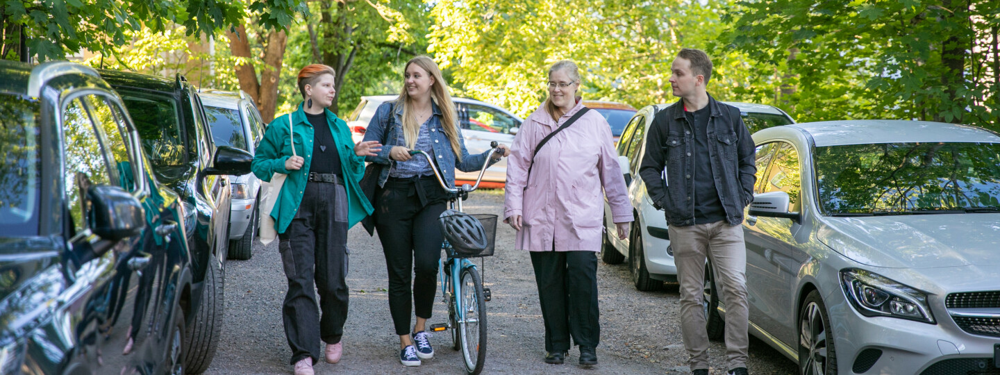 Four people walking towards the camera, one is walking with a bicycle.