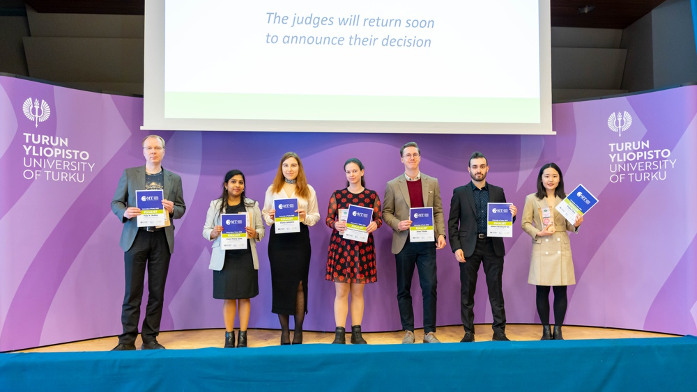 Kilpailun seitsemän finalistia seisovat lavalla käsissään finalisti-diplomit.