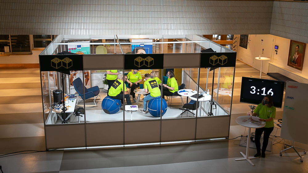 Kuusi henkilöä kuution sisällä ratkomassa ongelmia Science Battle -kilpailussa.