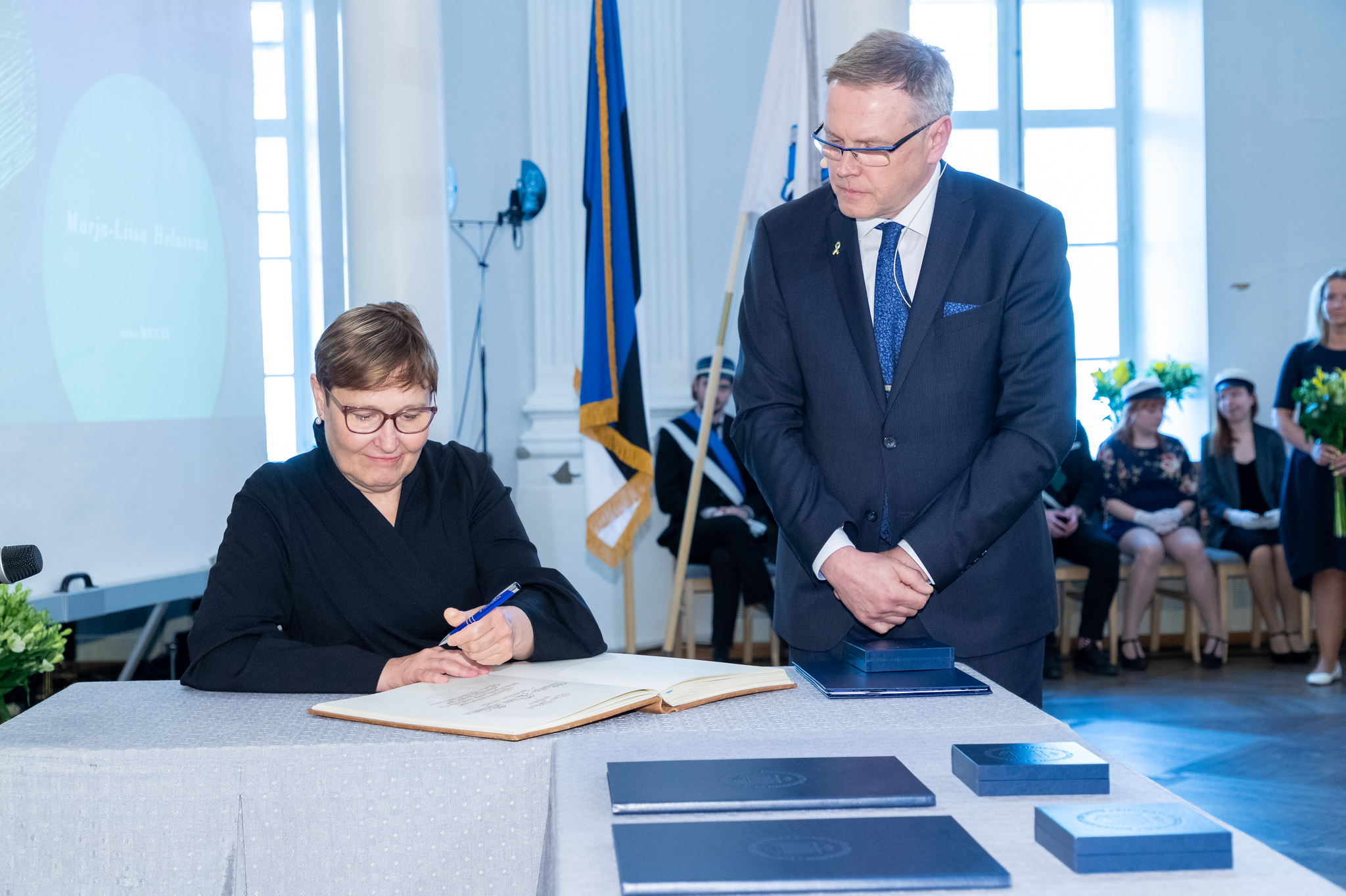 Suomen kielen professori Marja-Liisa Helasvuo allekirjoittaa promootiotodistusta. Vieressä Tarton yliopiston akateeminen sihteeri Tõnis Kärki.