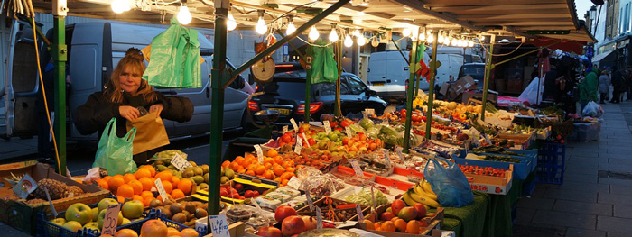 nainen torilla myymässä hedelmiä ja vihanneksia