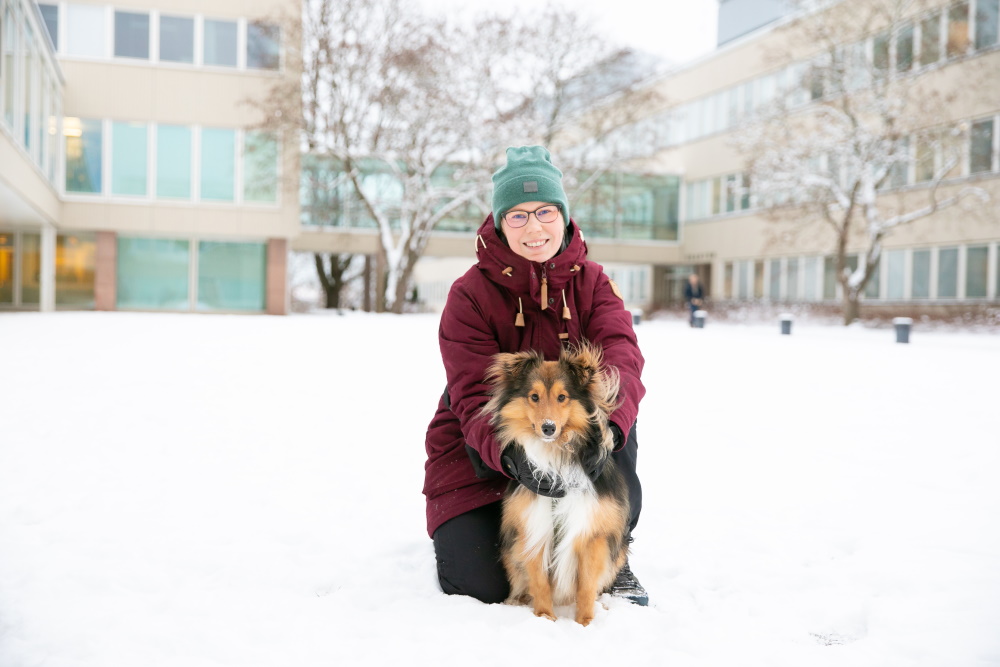 Milla Salonen yliopistonmäellä lumisessa maisemassa koiransa kanssa.