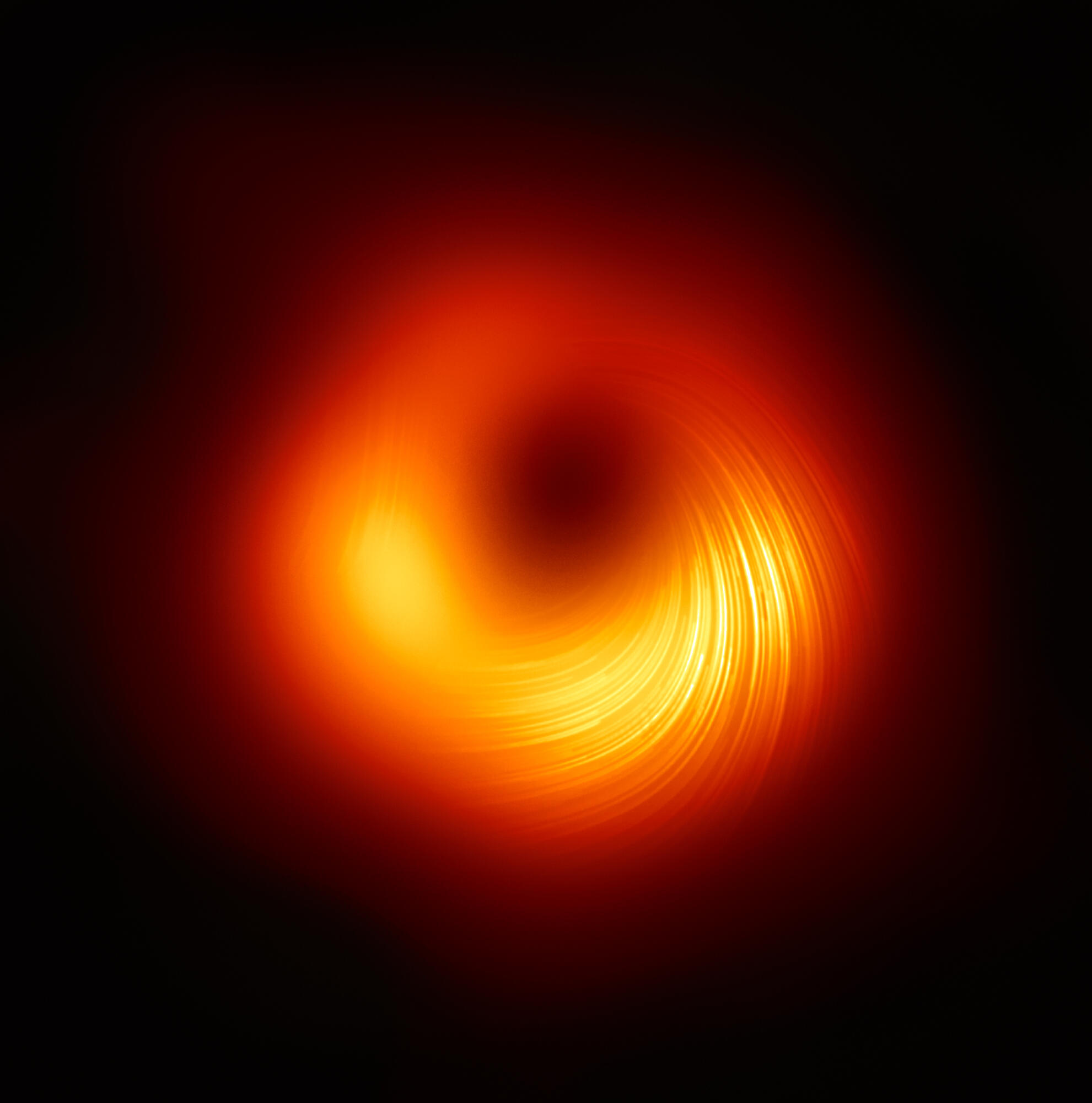 Messier 87 -galaksin keskellä oleva supermassiivinen musta aukko polarisoidussa valossa. Viivat osoittavat polarisaation suunnan, joka määräytyy mustan aukon magneettikentän suunnasta. Kuva: EHT Collaboration