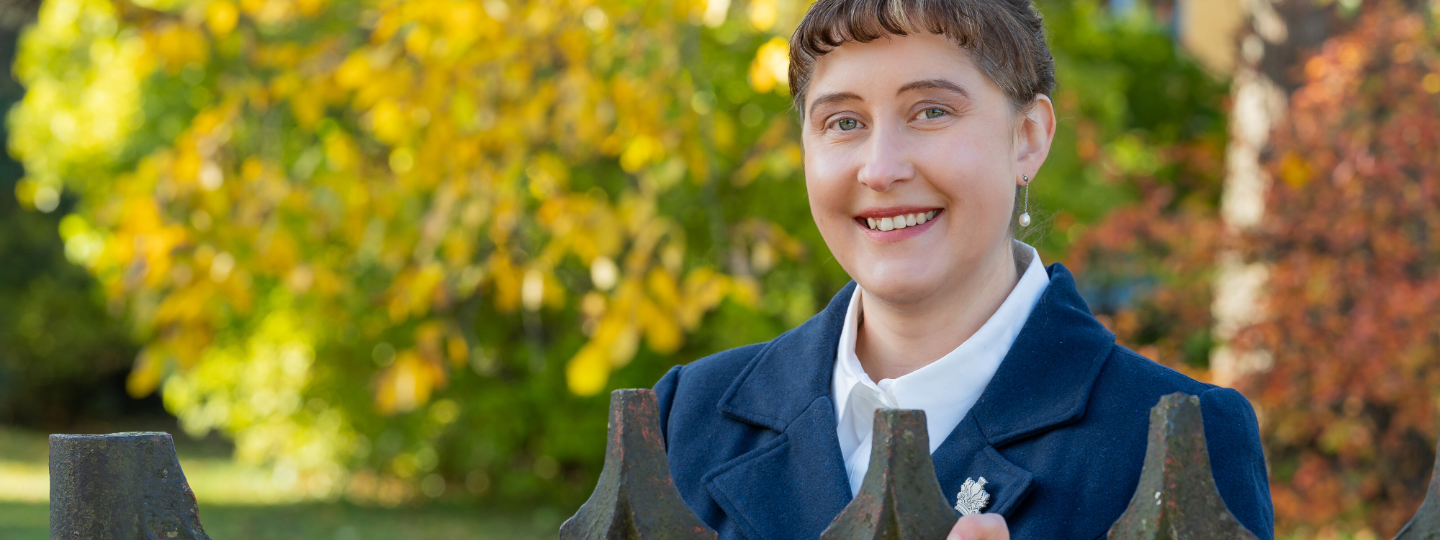 Ulla Ahlmen-Laiho lähikuvassa ulkona vanhan rautaisen portin edessä, taustalla näkyy puita joissa on värikkäät lehdet.