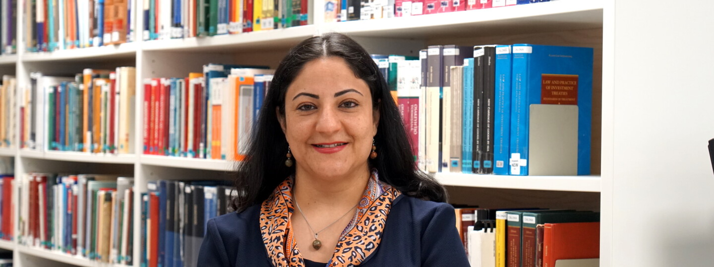 Tutkijatohtori Mehrnoosh Farzamfar oikeustieteellisen tiedekunnan kirjastohyllyjä taustallaan