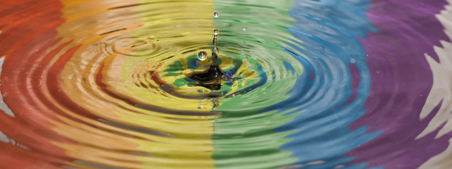 Vesipisara aiheuttaa veden pinnalle väreitä. Veteen heijastuu sateenkaaren värit.