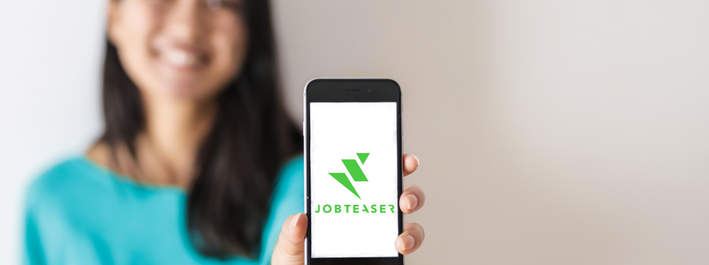 Henkilö näyttää älypuhelinta, jonka näytöllä on JobTeaserin logo