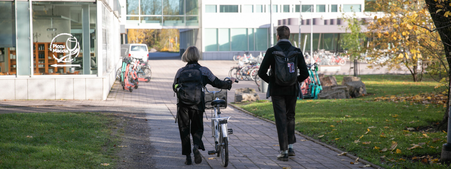 Kaksi opiskelijaa kävelemässä yliopiston kampuksella.