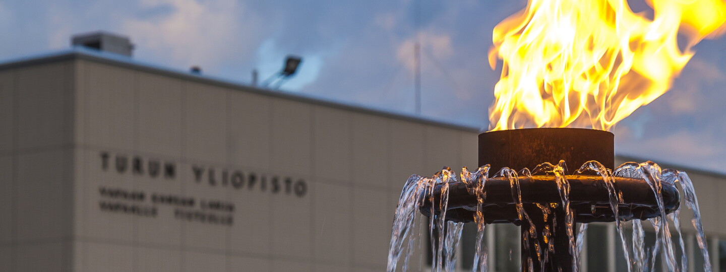 Etualalla suihkulähteen soihtu palamassa, taka-alalla Turun yliopiston päärakennus.