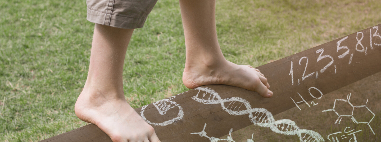 Lapsen tasapainoilee puomilla, kuvassa näkyvät vain jalat ja jalkojen edessä on erilaisia kaavoja