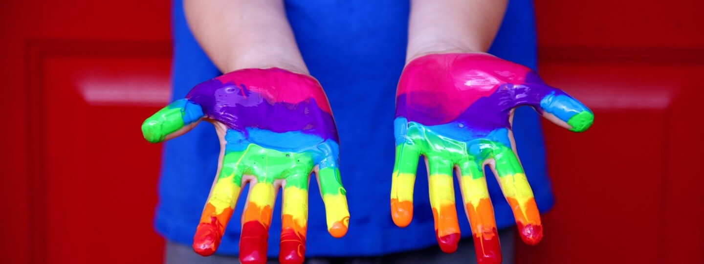 Lapsen kädet maalattuna sateenkaaren eri värein.
