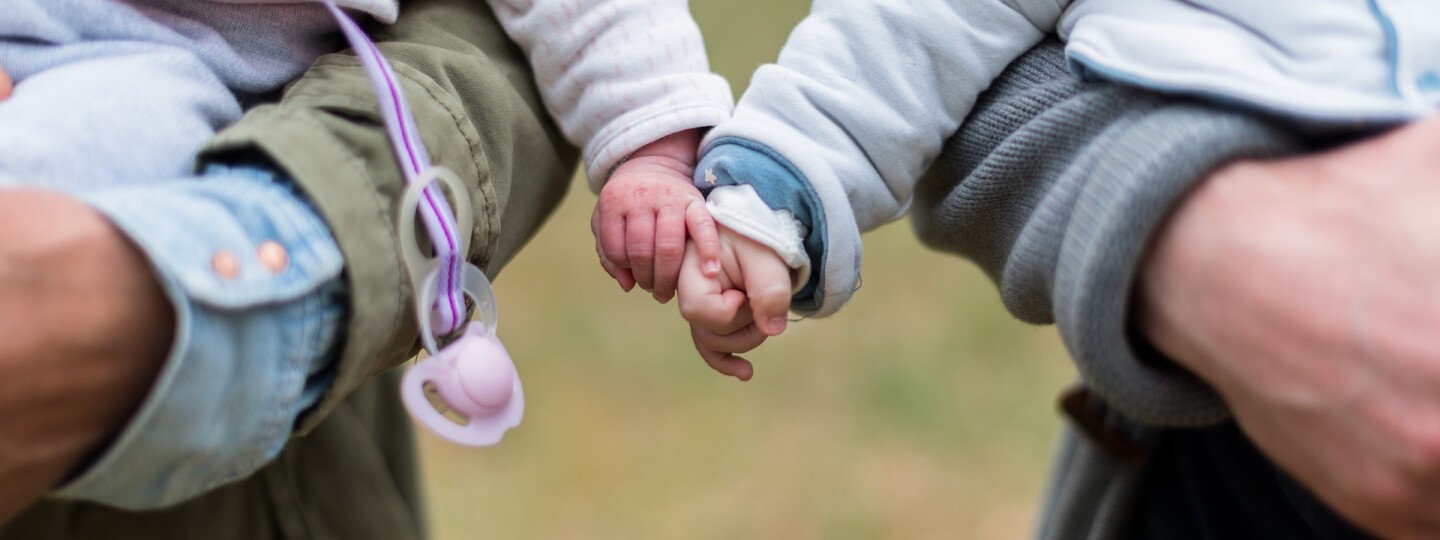 Kuvituskuva, jossa kaksi vauvaa kahdessa eri sylissä. Pitävät toisiaan kädestä. Henkilöistä näkyy vain kädet.