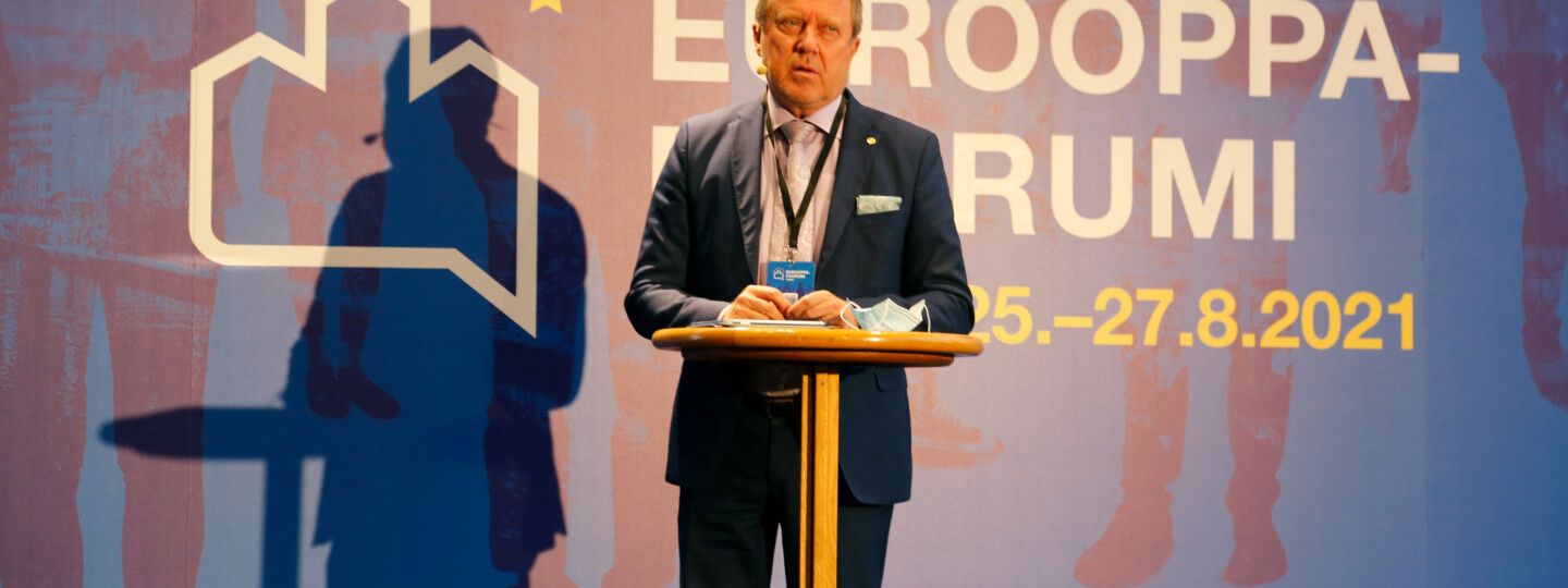 Jukka Kola Eurooppa-foorumin seinän edessä lavalla.