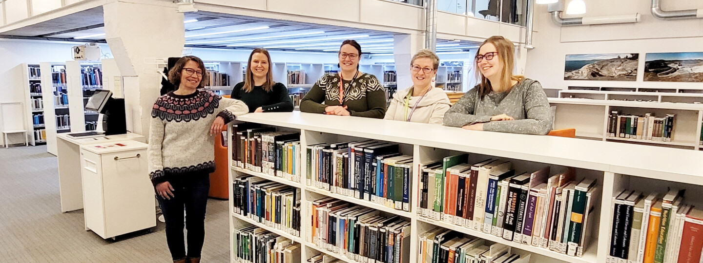 Five library staff members stand smiling behind a low bookshelf