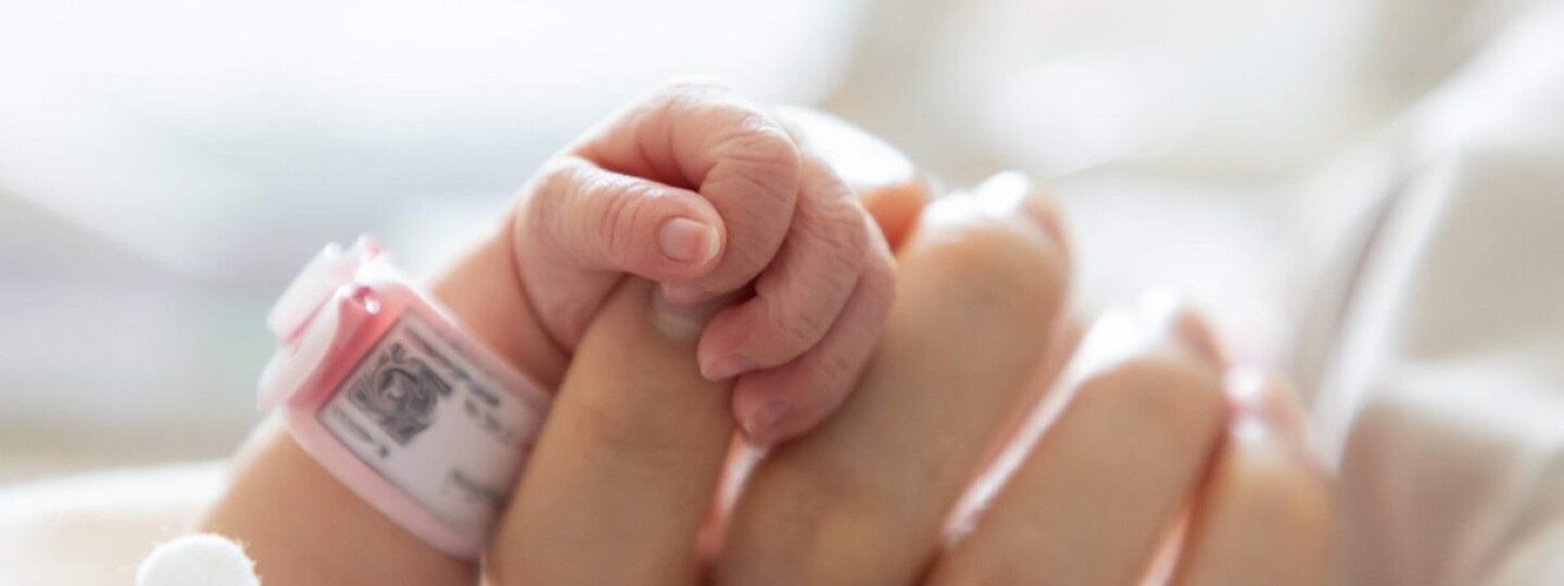 Vauvan sormet pitävät kiinni aikuisen kädestä.