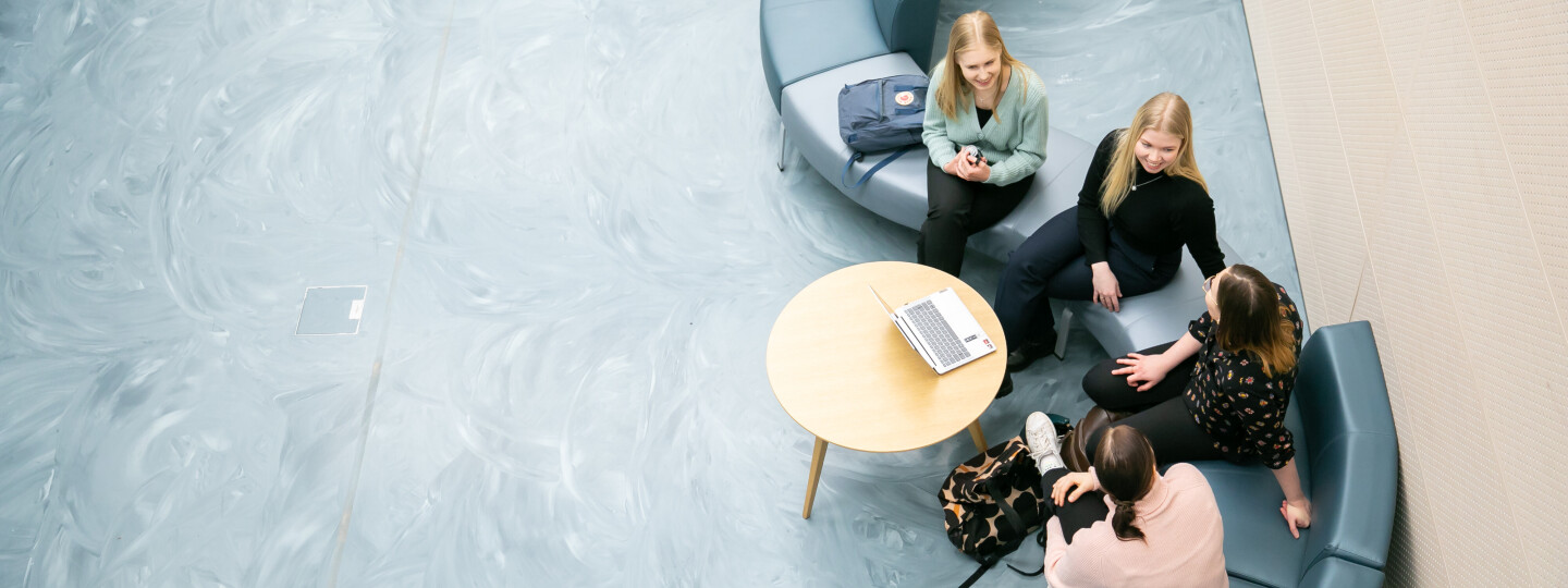 Opiskelijoita istumassa penkillä aulassa, kuva otettu ylhäältä päin