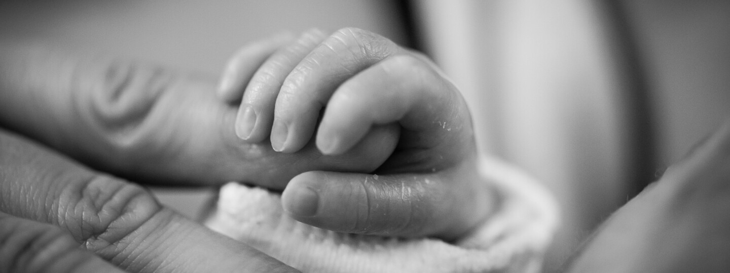 Mustavalkoinen kuva vauvan kädestä pitämässä kiinni aikuisen sormesta
