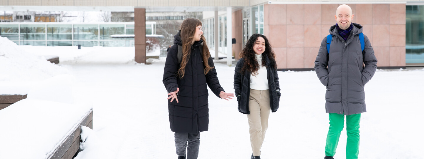 three people walking together in winter with university of turku main building in the background