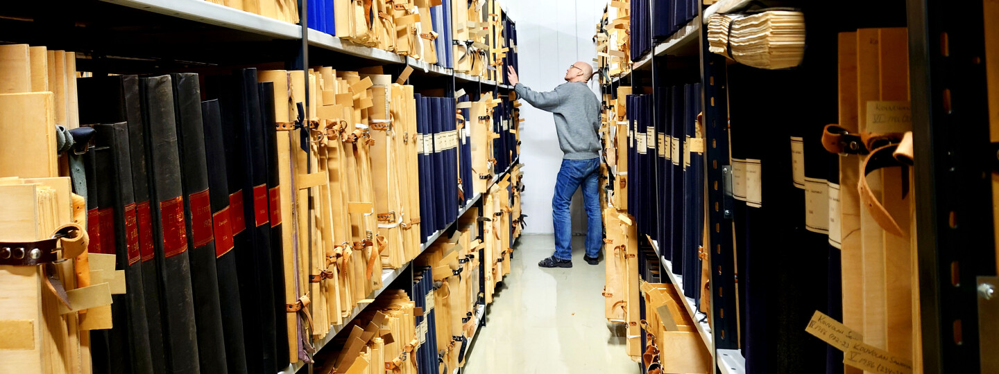 A librarian examines old newspapers bound in folders between shelves
