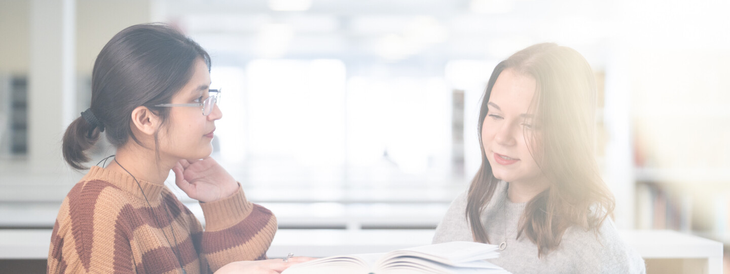 Kaksi henkilöä tutkimassa kirjaa kirjastossa