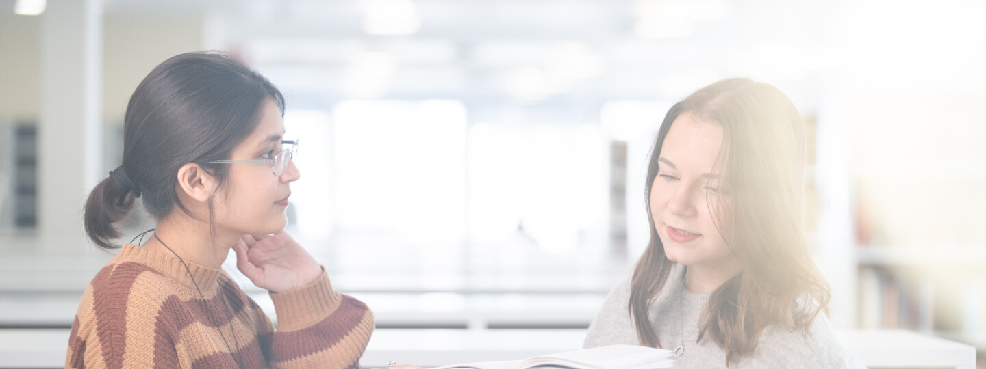 Kaksi henkilöä tutkimassa kirjaa kirjastossa