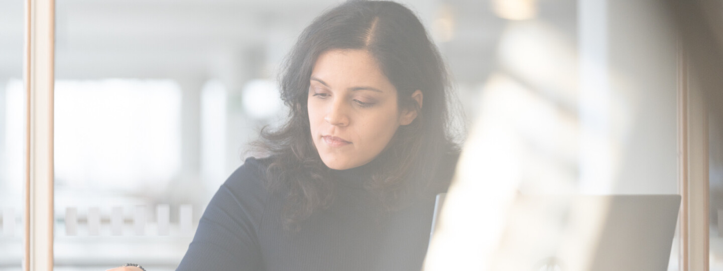 Henkilö työskentelemässä läppärillä ja selaamassa kirjaa