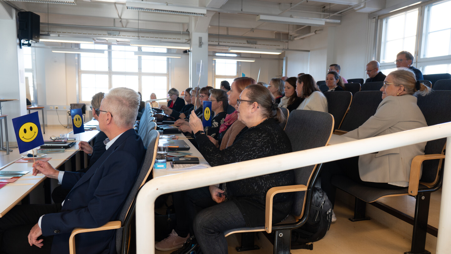 Ihmisiä istumassa yleisössä ja nostamassa värikkäitä lätkiä ilmaan. Lätkässä näkyy hymynaama.