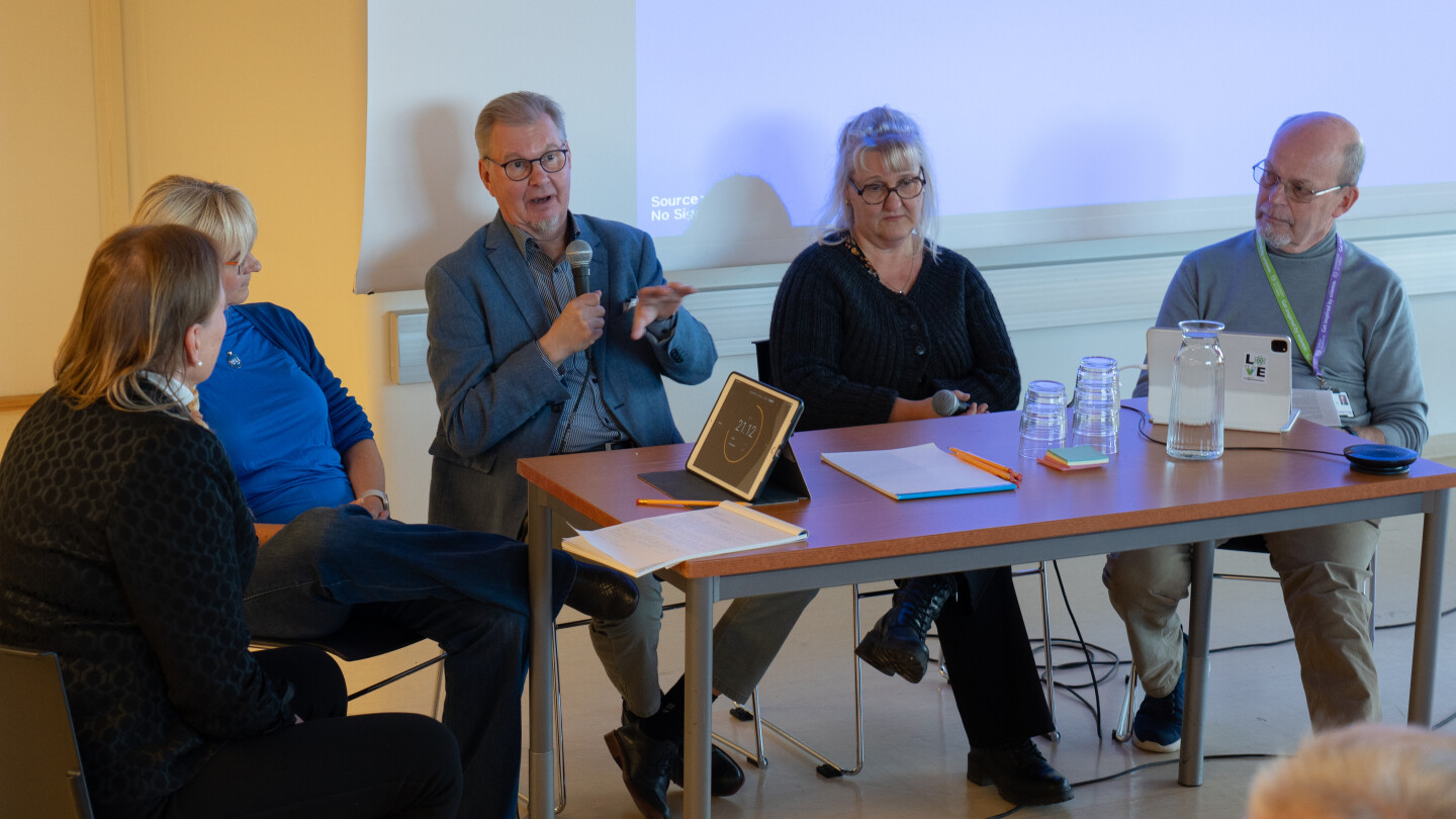 Ihmisiä puhumassa salin edustalla paneelissa