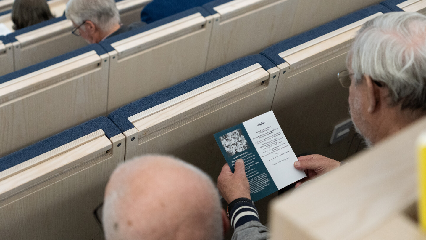 Luentosalissa istuva mies tarkastelee käsiohjelmaa