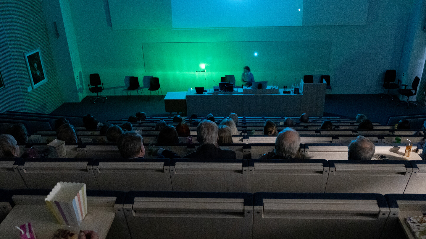 Ihmiset istuvat pimeässä salissa, kankaalla alkamassa elokuva