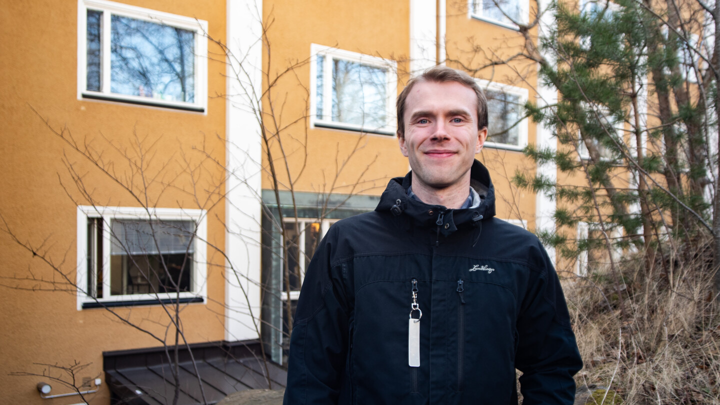 Tutkija kuvattuna ulkona keltaisen kerrostalon edustalla