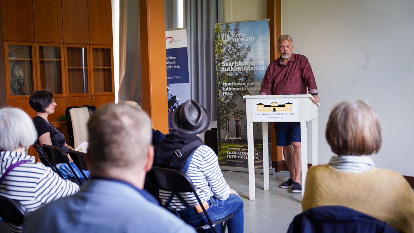 Jari Hänninen seminaarisalin edessä puhujapöydän äärellä puhumassa yleisölle