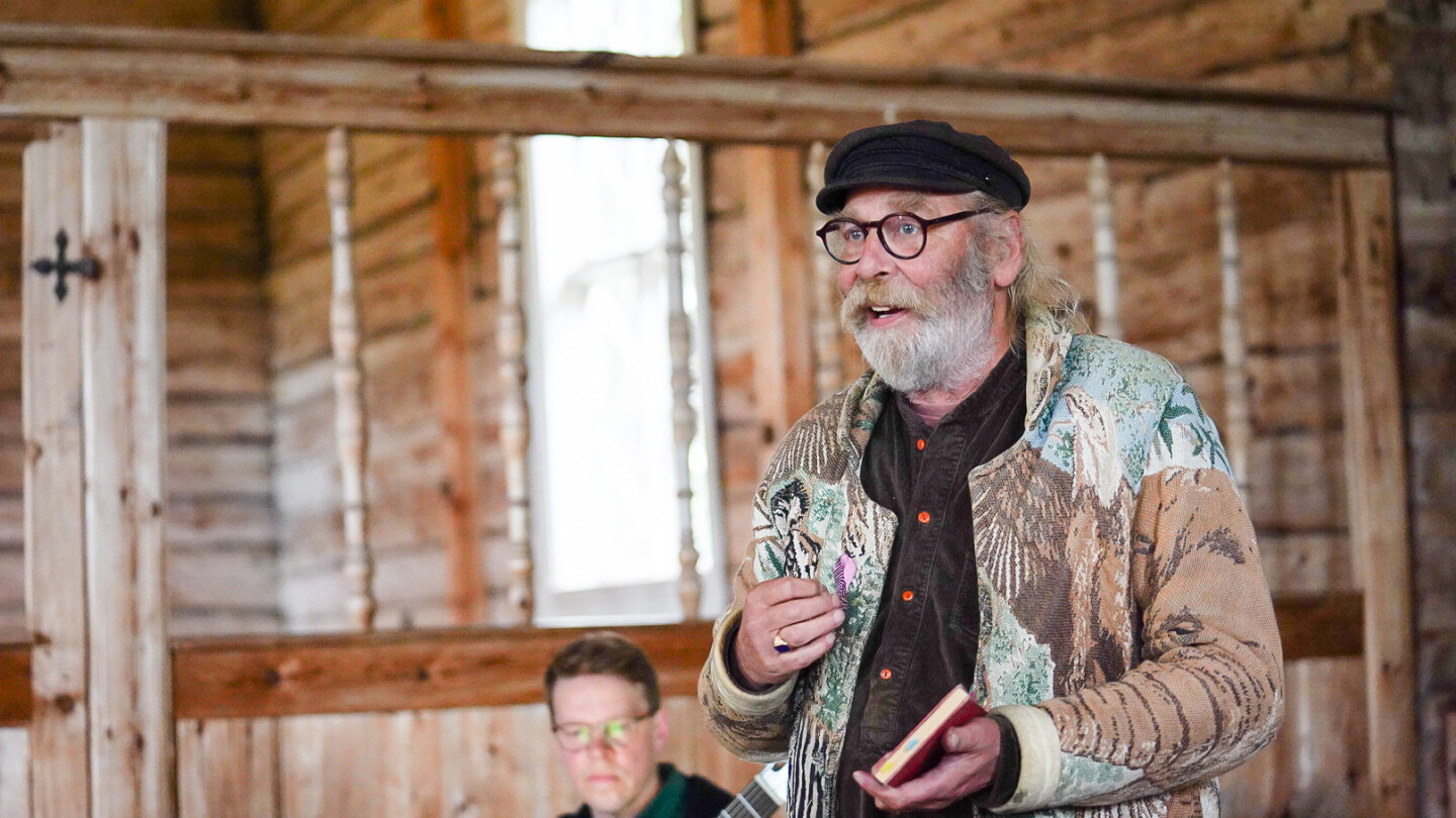 Kuvan etualalla lähikuvassa näyttelijä Vesa Vierikko esiintymässä Seilin kirkossa, ja Vierikon takana kitarataiteilija Petri Kumela soittaa kitaraa