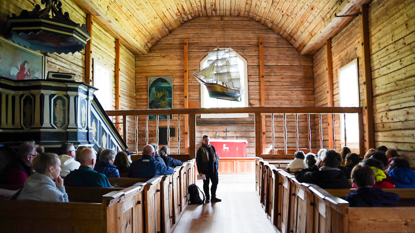 Tutkija Sofia Paasikivi seisoo Seilin vanhan puukirkon penkkirivien välissä yleisön edessä ja yleisö kuuntelee kun tutkija kertoo kirkon kryptoista