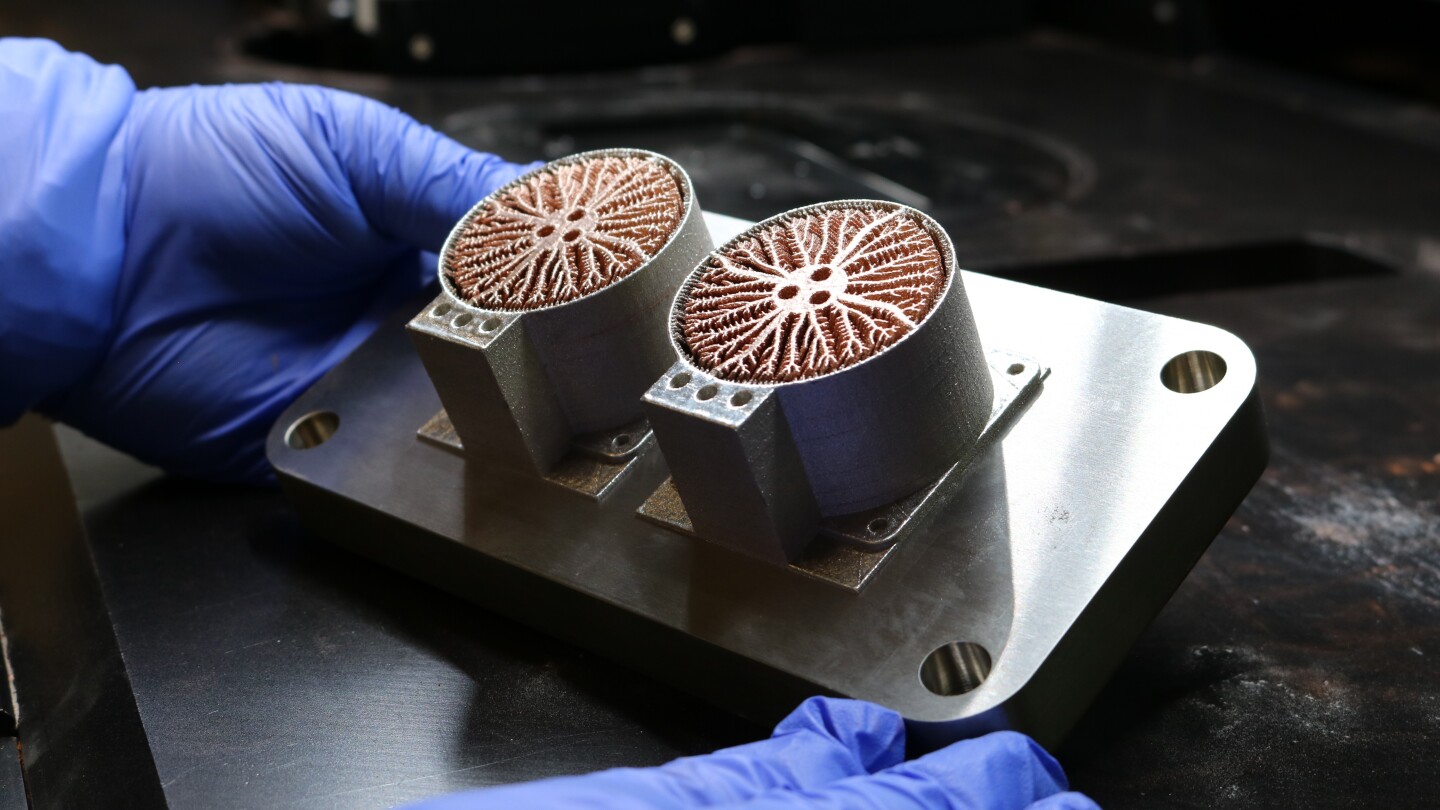Person holds a silver-coloured metal model component with two circular tubes that have bronze-coloured, root-like metal print inside.
