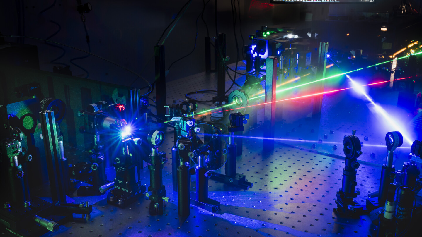 Dark laboratory setting where four different coloured lasers point to different directions, emanating a blue glow.