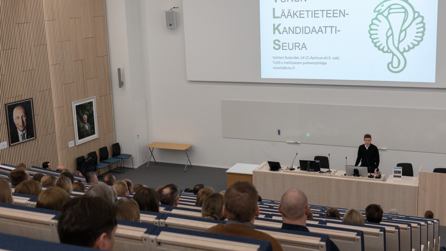 Henkilö puhumassa luentosalissa. Taululle on heijastettu Turun lääketieteen kandidaattiseuran logo