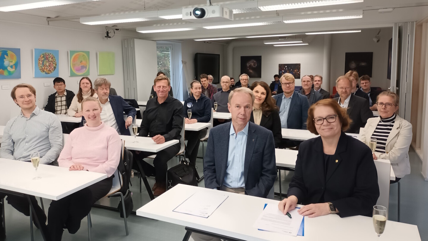 kokoushuoneellinen ihmisiä katsomassa kameraan iloisina