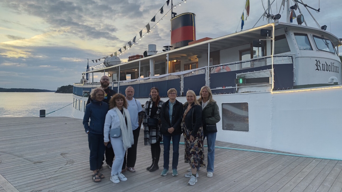 Kahdeksan ihmistä laiturilla laivan edessä.