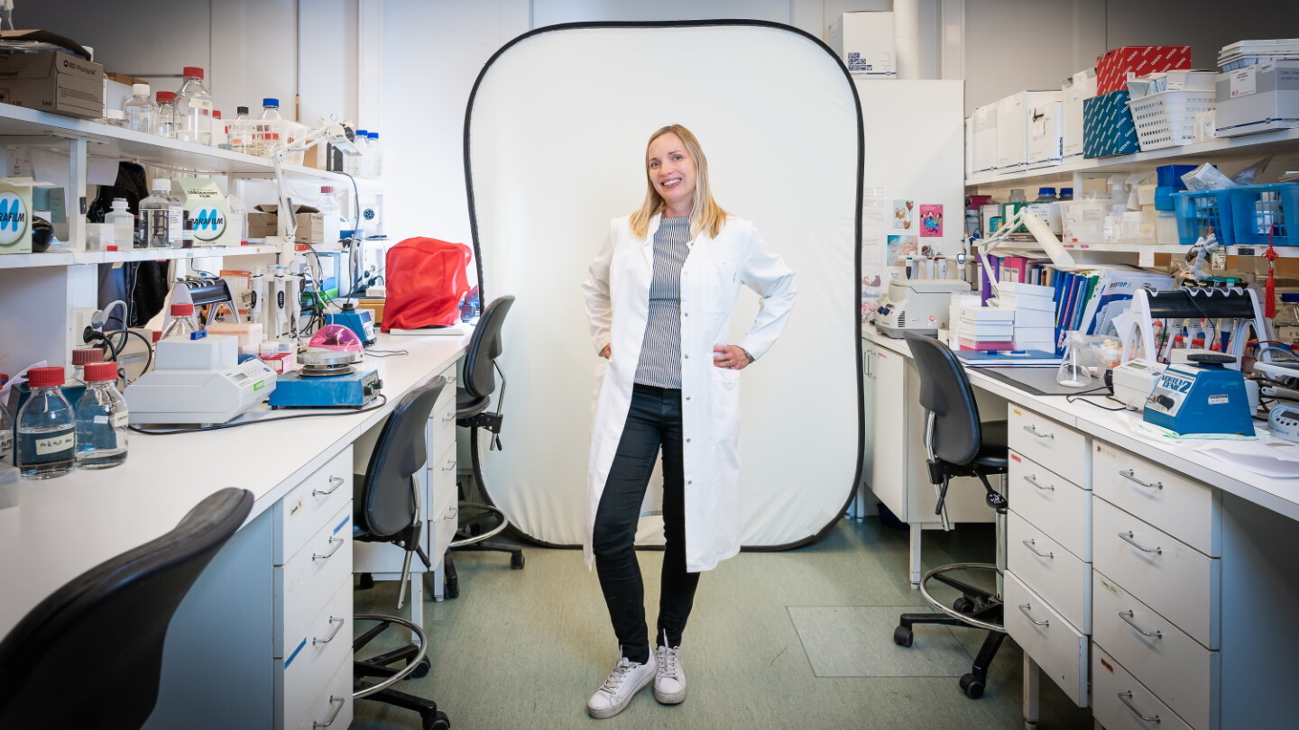 Maija Hollmén seisoo laboratoriossa ja katsoo kameraan