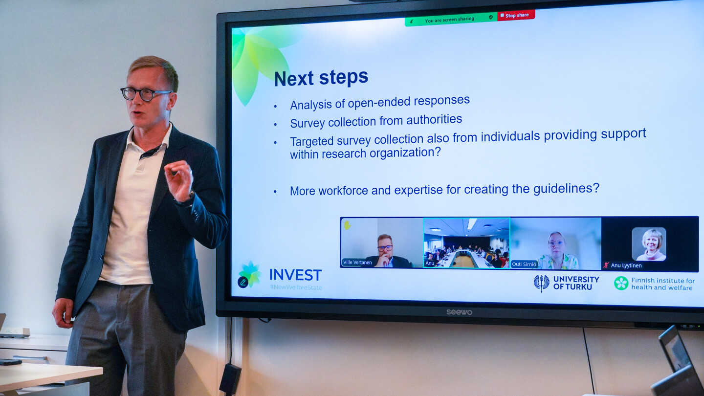 tutkija neuvottelutilan edessä ja etäyhteys näkyvissä.