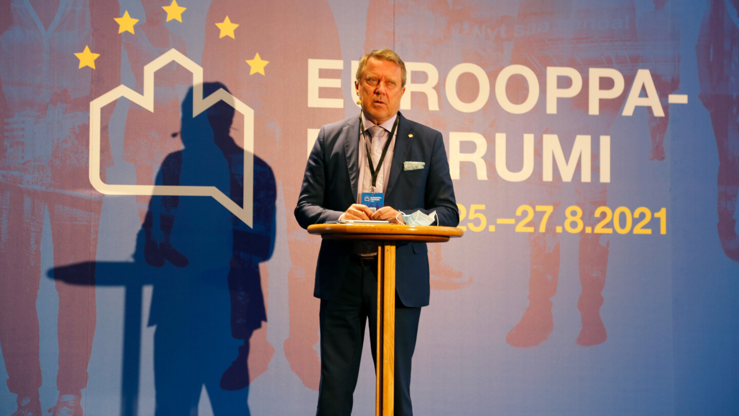 Jukka Kola Eurooppa-foorumin seinän edessä lavalla.