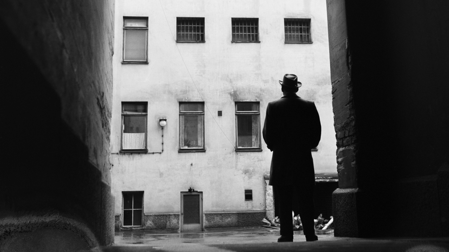 Mies seisoo synkässä kaupungin porttikongissa selin kameraan 1950-luvulla.