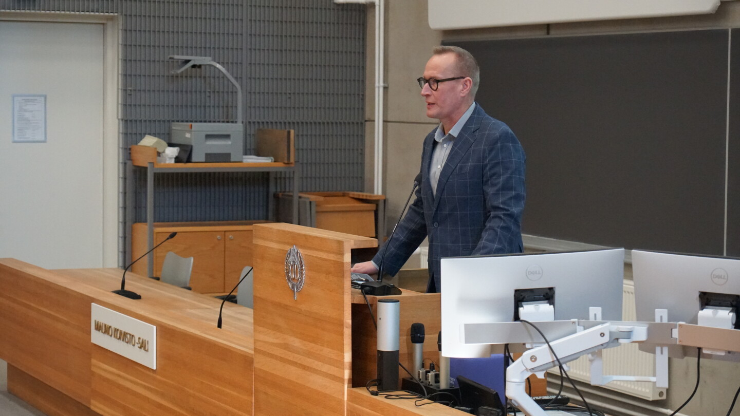 Mies puhumassa luentosalin edessä.