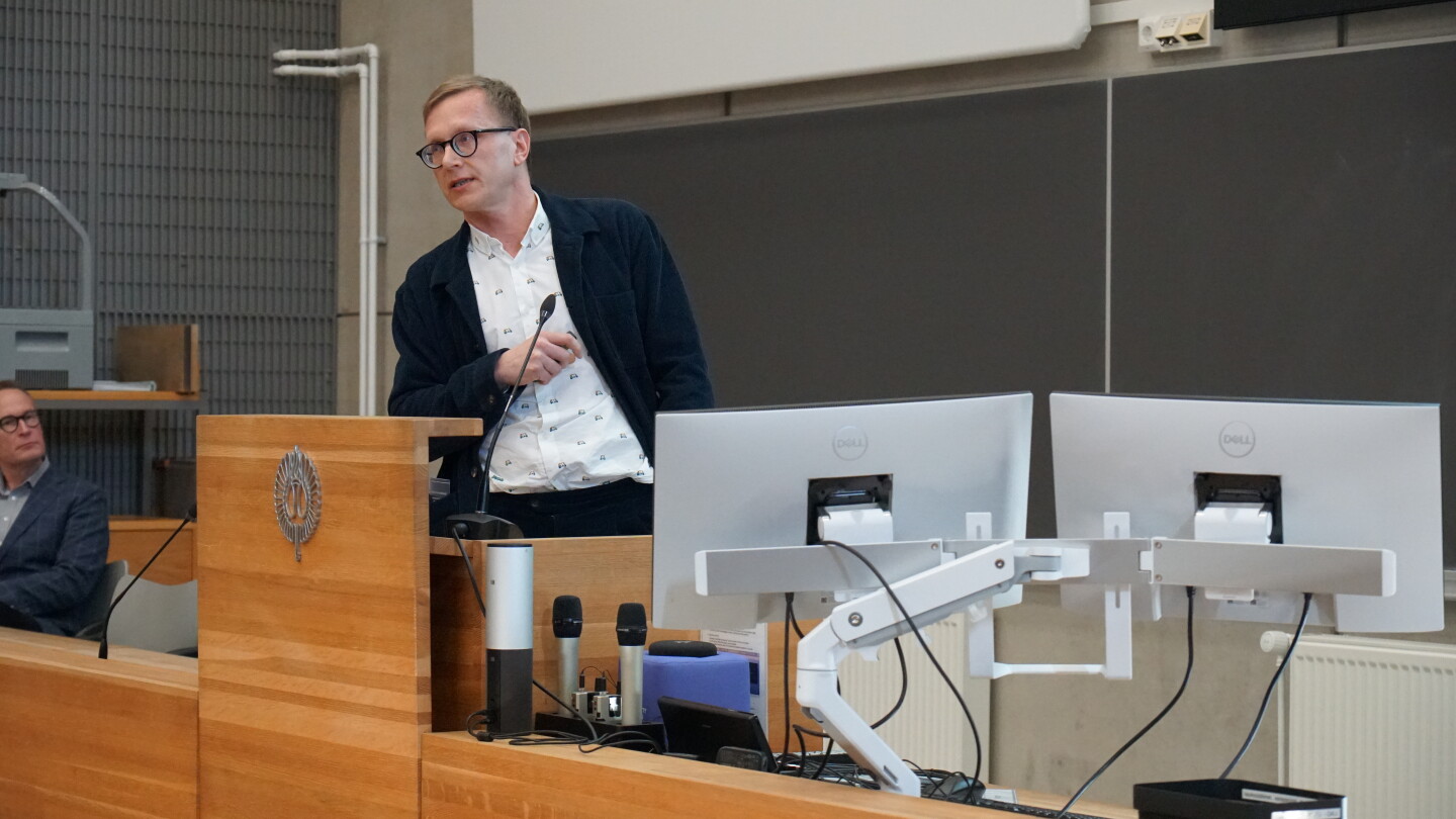 Mies puhumassa luentosalin edessä.