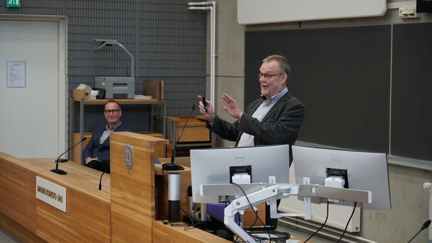 Mies puhumassa luentosalin edessä.