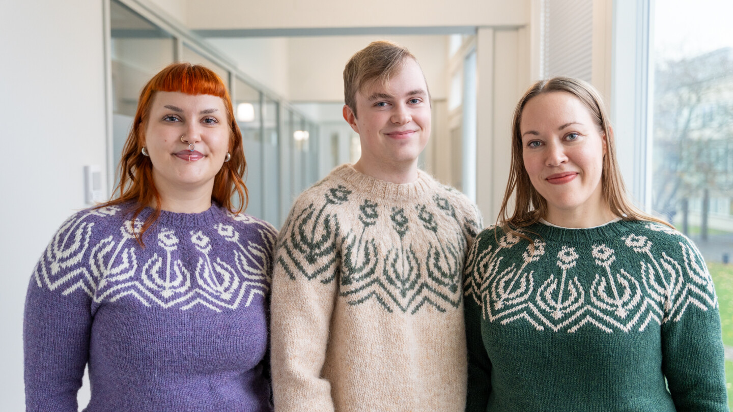 Kolme henkilöä Turun yliopiston soihtu-neuleet päällä.