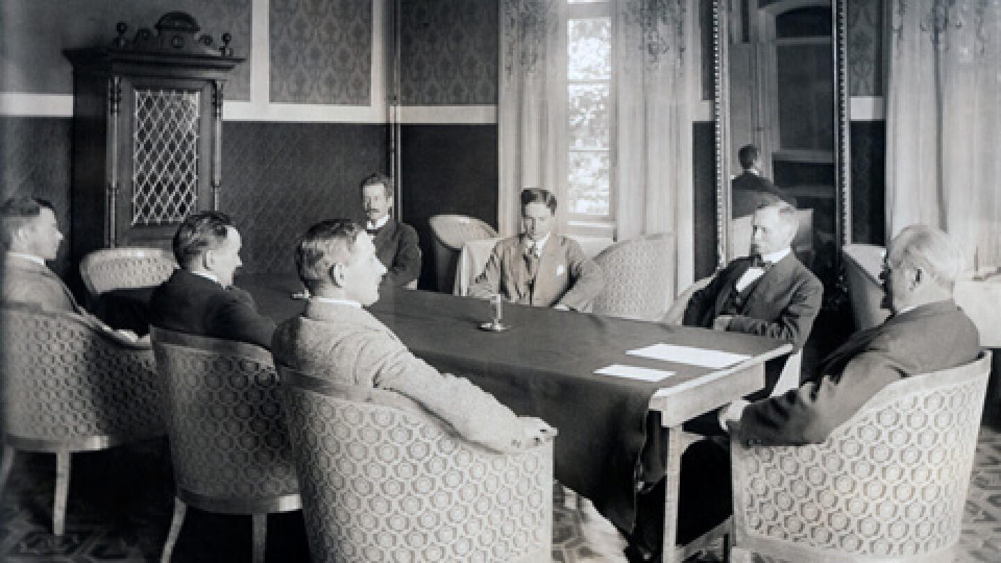 Yliopiston professoreja keväällä 1923 kokoontuneena opettajainhuoneeseen. Pöydän päässä rehtori A. H. Virkkunen, pöydän takana vasemmalta K. Linkola, E. Kaila, M. Palomaa, pöydän edessä vasemmalta K. Väisälä, V. A. Koskenniemi ja V. Linnaniemi.