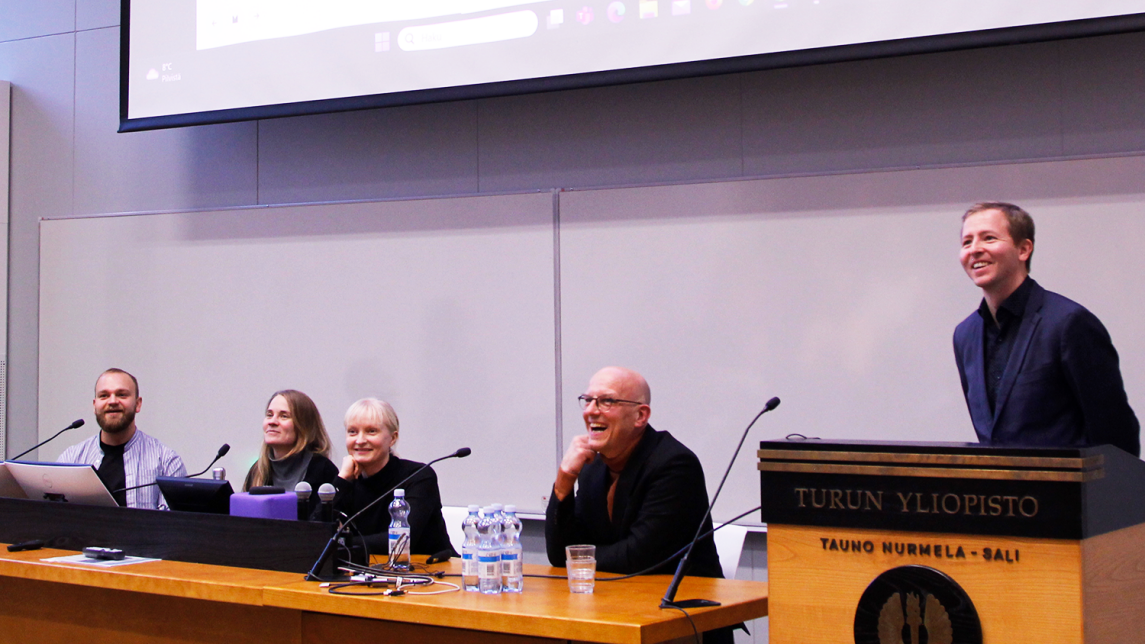 Kuvassa juhlaseminaarin paneelin keskustelijat ja juontaja luentosalin edessä