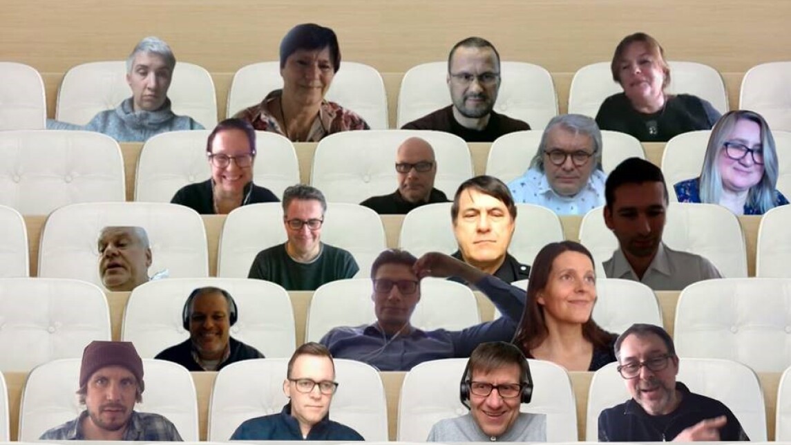 Screenshot of 19 people's faces put to sit in rows of white benches